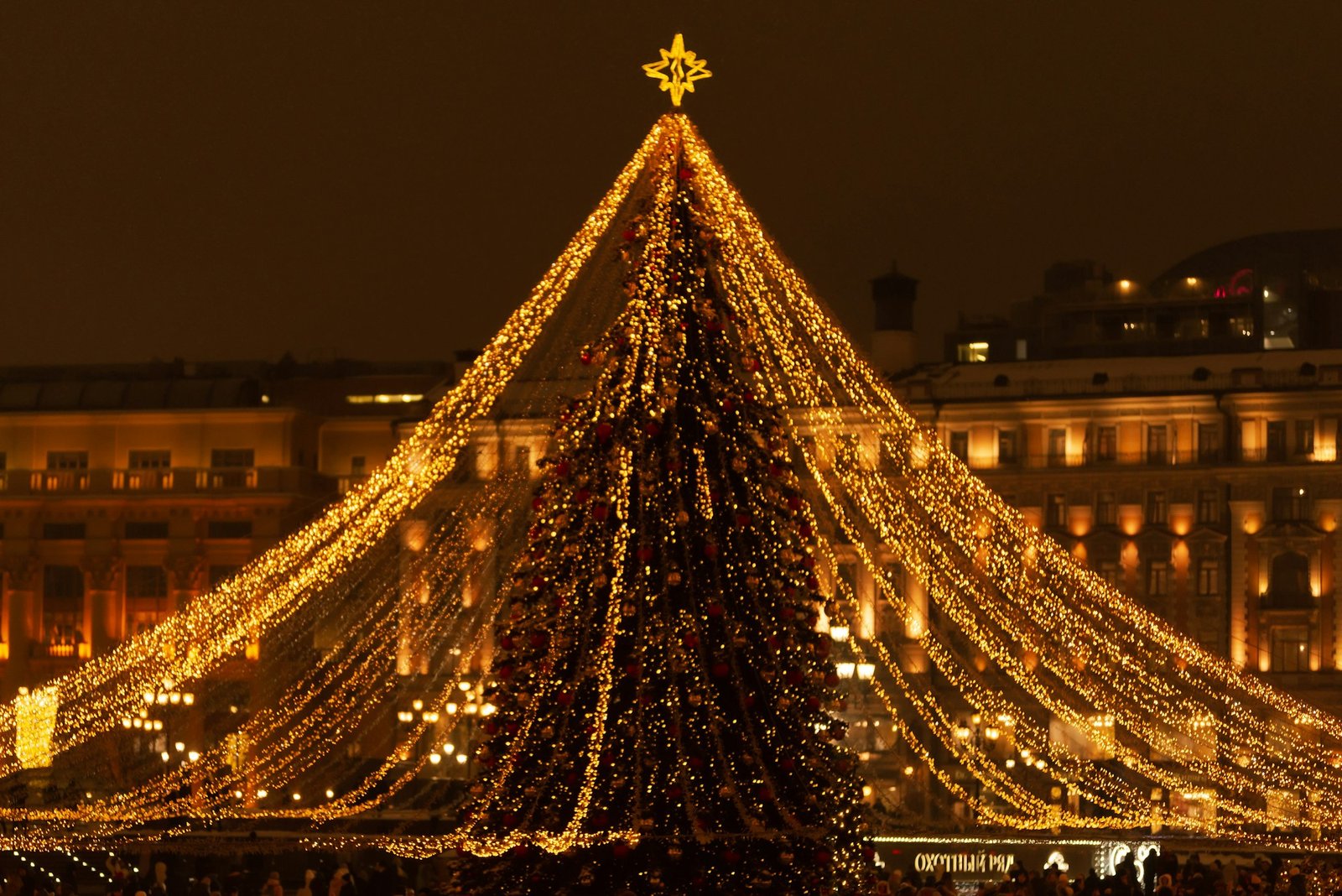 A large Christmas tree in the city center with golden lights on the background of the night city.