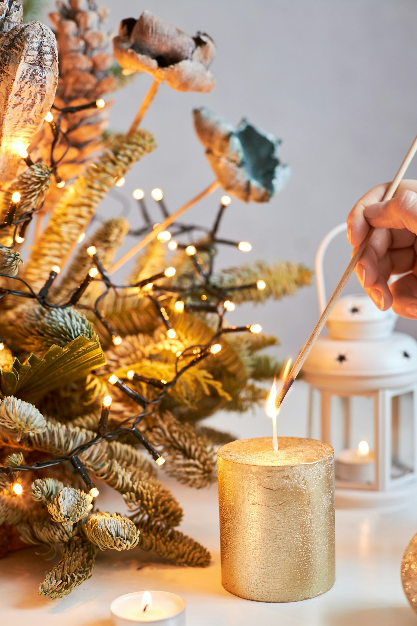 Close-up of the hands of a girl lighting a candle against the backdrop of a Christmas decoration