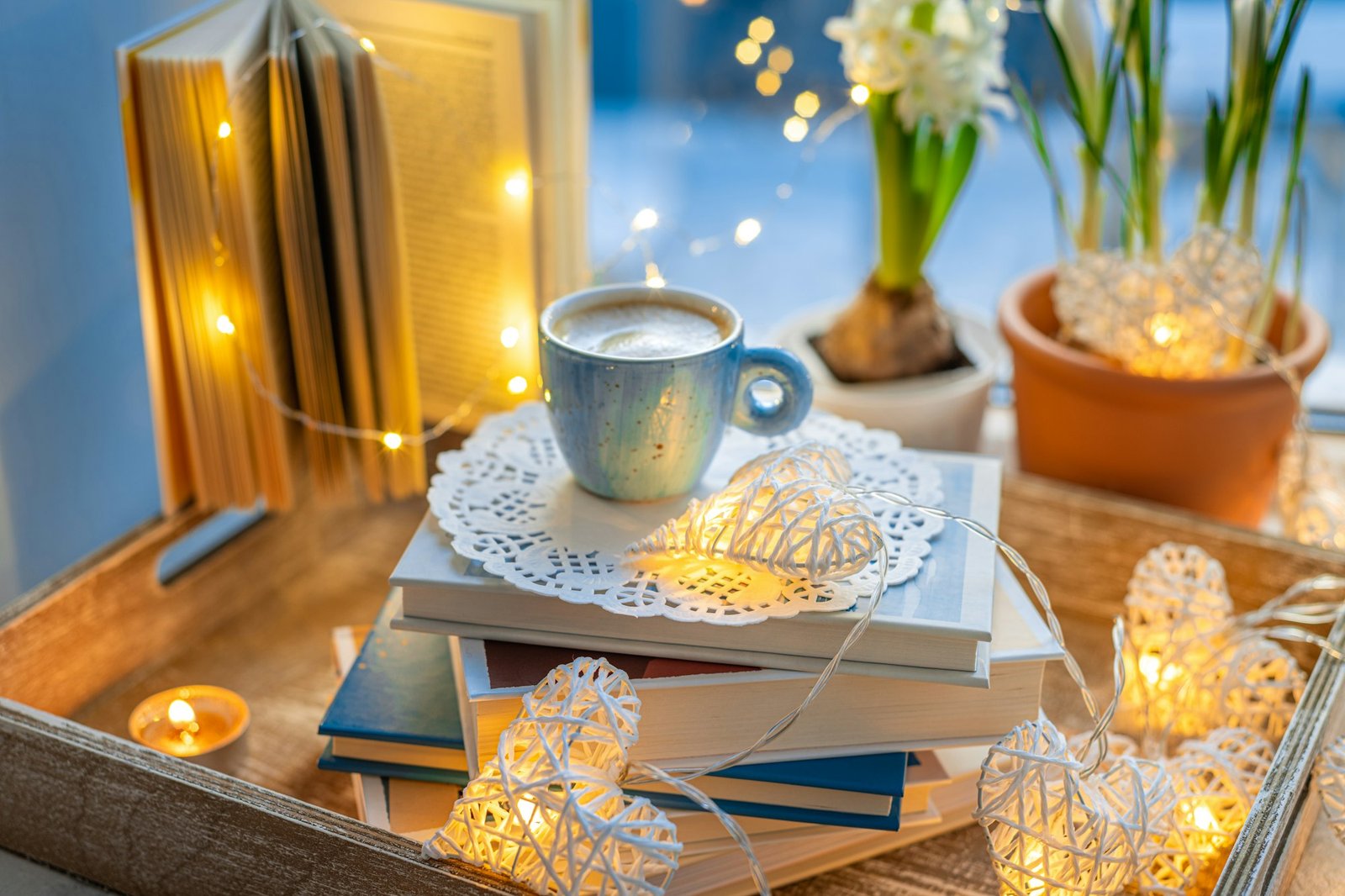 Coffee cup, open book, spring flowers, sparkle lighting garland on window sill