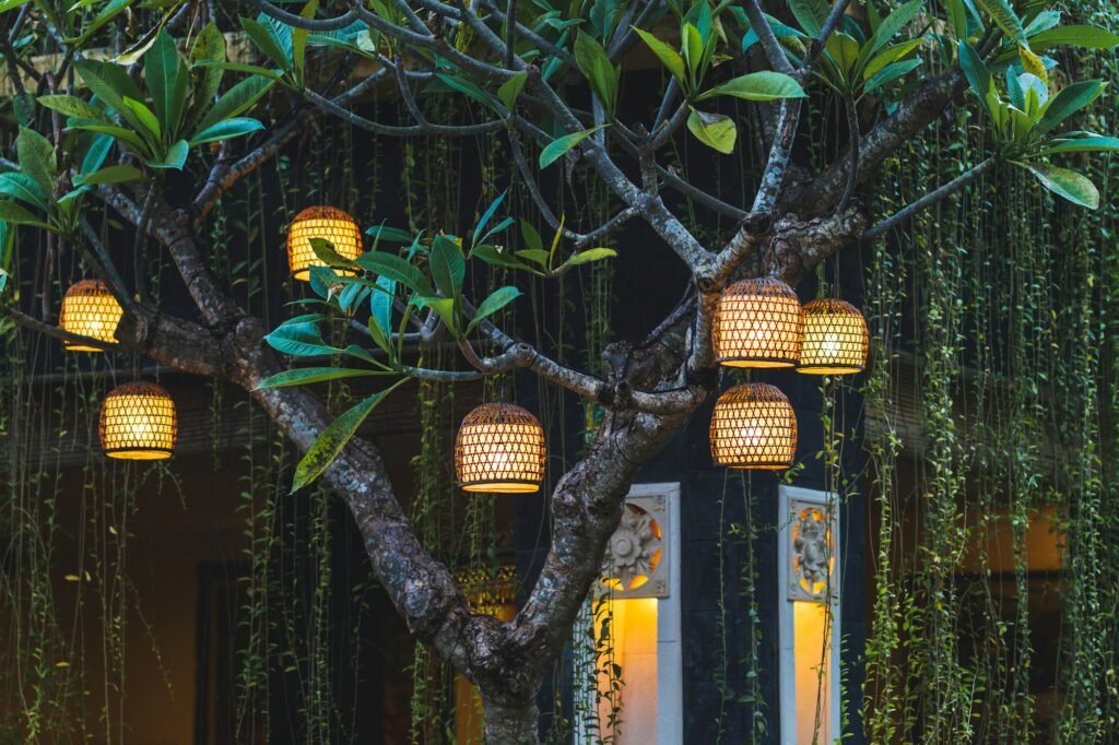 Many beautiful hahdmade wicker lamps hanging outside in garden on tree