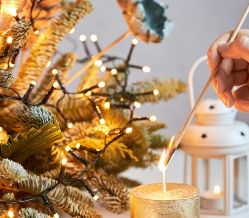 Close-up of the hands of a girl lighting a candle against the backdrop of a Christmas decoration