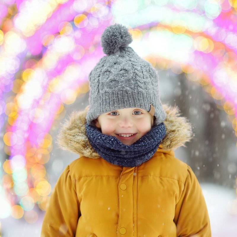 Little boy is admiring a large glowing street decoration on Christmas fair